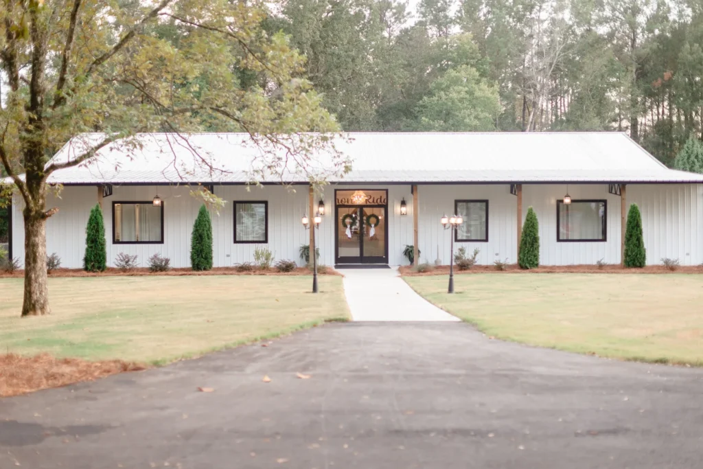 The front exterior of Lemon Ridge Events, a modern white 10,000-square-foot venue in Jasper, Alabama, featuring elegant black-trimmed windows, a crystal chandelier entryway, and manicured lawns leading to the main entrance.