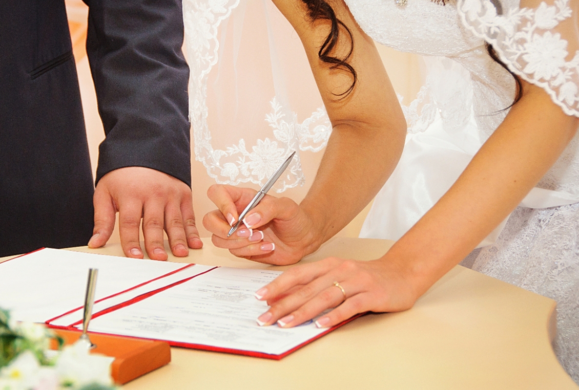 A close-up shot of a bride in a lace wedding dress signing official marriage documents in Jasper, Alabama. The groom stands beside her as they finalize their union at Lemon Ridge Events. This image captures a pivotal milestone celebrated in our versatile 10,000-square-foot facility and provides the ideal setting for both intimate micro weddings and large-scale celebrations for up to 250 guests. We ensure every detail, from the ceremony to the final signature, is effortless for couples throughout the Greater Birmingham and Tuscaloosa areas.