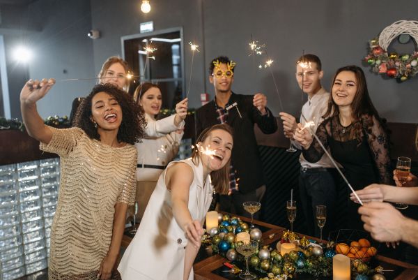A group of diverse colleagues celebrating at a festive corporate event, laughing while holding lit sparklers around a table decorated with champagne flutes and ornaments.