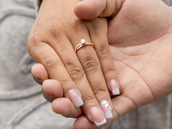 A close-up shot of a rose gold diamond engagement ring on a woman's hand, being held by a partner's hand, symbolizing a romantic proposal.